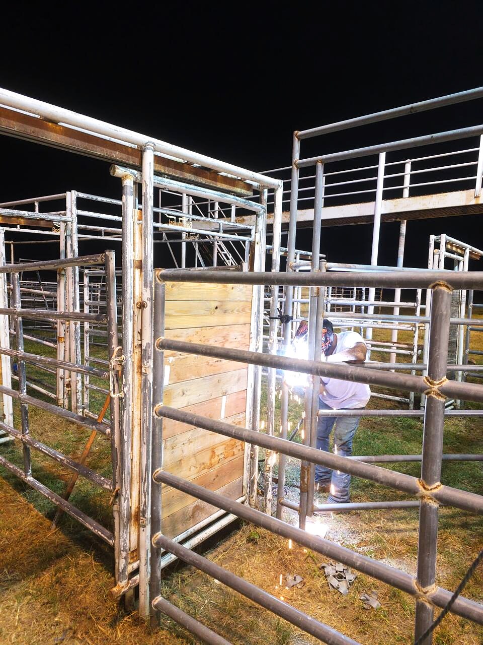 Arena crew welding metal livestock pens at night